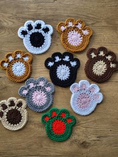 six crocheted animal paw prints on a wooden surface, all in different colors