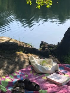 a book and some shoes on a blanket by the water