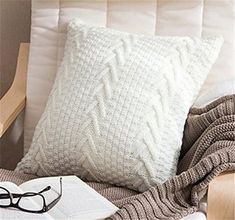 a white pillow sitting on top of a wooden chair next to a book and blanket