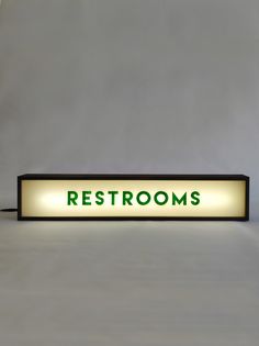 a sign with the word restrooms lit up in front of a white wall and floor