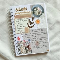 an open spiral notebook with pictures and words on the cover, sitting on top of a white sheet