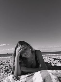 a woman laying on top of a beach next to the ocean with her hands in her hair