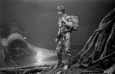 black and white photograph of a man with a backpack standing in front of an airplane