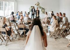 a woman in a wedding dress walking down the aisle with her back to the camera