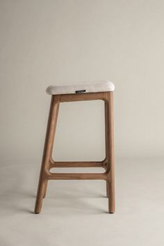 a wooden stool with a white cushion on the seat and backrest, against a gray background