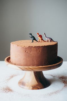 two small toy dinosaurs on top of a chocolate cake