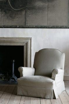 a chair sitting in front of a fireplace with a painting on the wall behind it