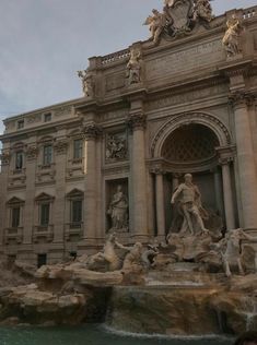 people are standing in front of a building with statues on the sides and water running through it