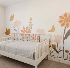 a white crib in front of a wall with flowers painted on it and a bed