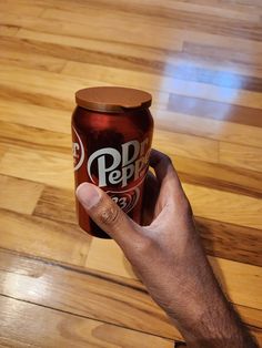 a hand holding a can of pepsi on top of a wooden floor