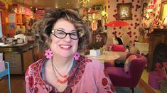 a woman with glasses is sitting in a room full of furniture and decor, smiling at the camera