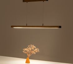 an orange vase with flowers in it on a white surface under a light fixture that is suspended from the ceiling