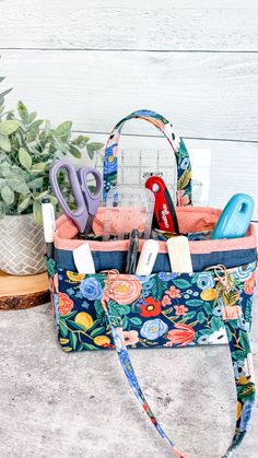 a purse with scissors and other items in it sitting next to a potted plant