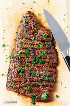 a piece of steak on a cutting board with a knife and parsley sprig