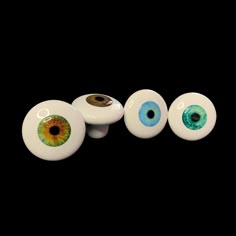 four white ceramic eyeballs with green and yellow irises on them, against a black background