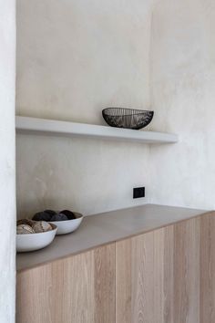 two bowls sit on top of a shelf in the corner of a room with white walls