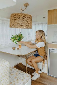 a woman sitting at a kitchen table with plants in her hand and a potted plant on the counter