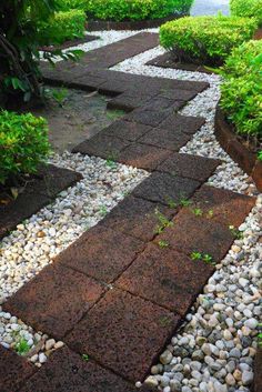 a walkway made out of stones and gravel in the middle of a garden with trees