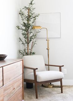 a white chair sitting next to a wooden dresser in a room with a lamp on it