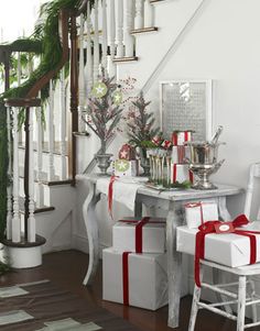 christmas decorations and presents are on the table in front of the stair case, which is decorated with greenery