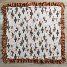 a brown and white cactus print blanket with ruffles on the edges, sitting on a wooden floor