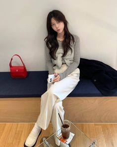 a woman sitting on top of a glass table next to a red purse and cup