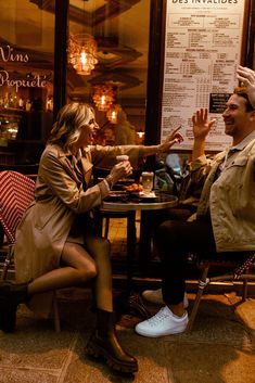 a man and woman sitting at a table in front of a restaurant talking to each other