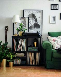 a green couch sitting next to a book shelf filled with vinyl records and potted plants