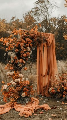 an outdoor ceremony with orange flowers and drapes on the ground, surrounded by tall dry grass