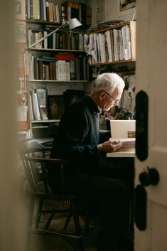 an older man sitting at a desk in front of a book shelf