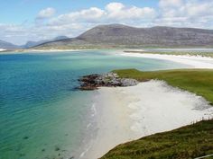 an aerial view of a sandy beach and ocean with mountains in the backgroud