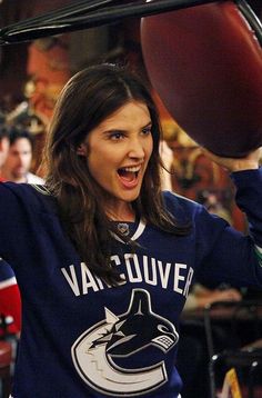 a woman holding a football in her right hand and wearing a vancouver hockey jersey on