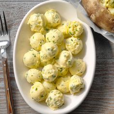 a white bowl filled with potato salad next to a fork and knife on a wooden table