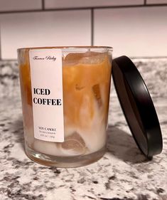 an iced coffee in a glass on a marble counter top with a black lid next to it