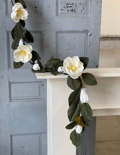 white flowers and green leaves are arranged on the mantle