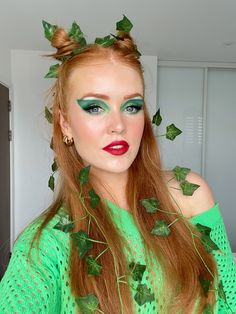 a woman with long red hair wearing green makeup and ivy leaves on her head is posing for the camera