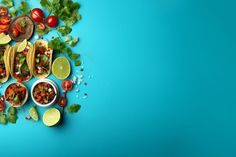 tacos, limes and tomatoes are arranged on a blue background with cilantro