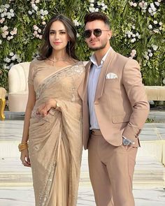 two people standing next to each other in front of a flower covered wall with white flowers