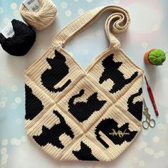 a crocheted bag with cats on it next to yarn and scissors