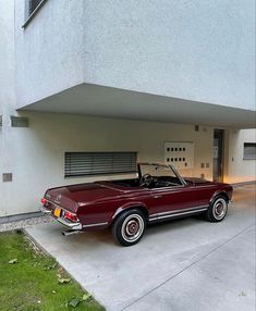 a red car parked in front of a white building with an open garage door on the side