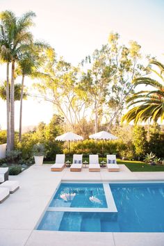 an outdoor swimming pool with lounge chairs and umbrellas in the shade, surrounded by palm trees