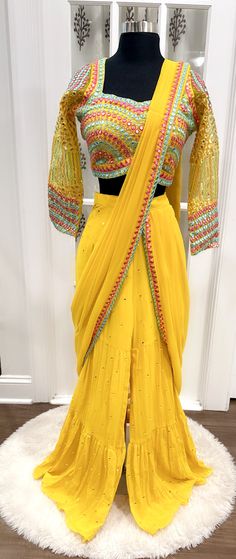 Step into elegance with this chic and trendy Haldi yellow Sharara set, adorned with stunning mirror work. Crafted from lightweight Georgette, this size 40/42 ensemble offers a contemporary look with traditional flair. Perfect for those special occasions when you want to stand out Anarkali Sets With Dori Work On Chinon, Navratri Georgette Set With Dupatta, Bollywood Style Sets With Dori Work In Chinon, Chinon Sets With Dabka Work In Traditional Drape, Yellow Semi-stitched Sets For Navratri, Bollywood Style Chinon Sets With Dori Work, Bollywood Chinon Sets With Dori Work, Yellow Chinon Sets For Wedding, Gold Georgette Set With Mirror Work