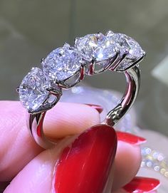 three stone diamond ring being held by a woman's hand with red nail polish