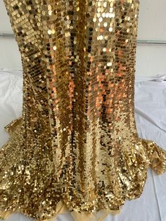 gold sequin top with ruffles on the shoulders and bottom, sitting on a white sheet