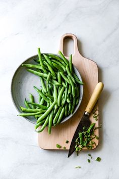 green beans in a bowl with a knife on a cutting board next to it,