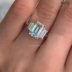 a woman's hand holding an emerald and diamond ring