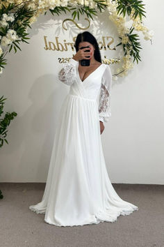 a woman taking a selfie in front of a white backdrop with flowers and greenery