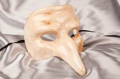 a white mask with a bird's head on it sitting on a silver cloth