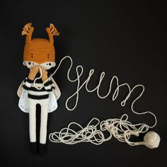 a crocheted doll next to a string and ball of yarn on a black background