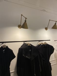 three lamps are hanging on the wall above some black shirts and jackets in a clothing store